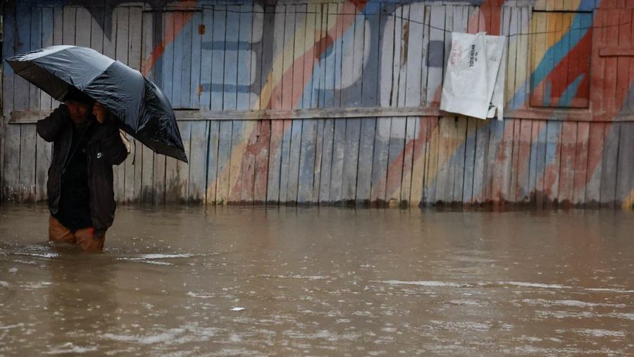 Seorang pria membawa payung berjalan melewati grafiti bertuliskan 'Nepal' di jalan yang banjir di sepanjang tepi Sungai Bagmati yang meluap setelah hujan lebat, di Kathmandu, Nepal, 4 Oktober 2025. (REUTERS/Navesh Chitrakar)