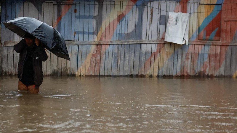 Seorang pria membawa payung berjalan melewati grafiti bertuliskan 'Nepal' di jalan yang banjir di sepanjang tepi Sungai Bagmati yang meluap setelah hujan lebat, di Kathmandu, Nepal, 4 Oktober 2025. (REUTERS/Navesh Chitrakar)
