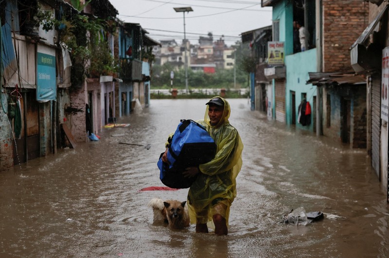 Seorang pria membawa payung berjalan melewati grafiti bertuliskan 'Nepal' di jalan yang banjir di sepanjang tepi Sungai Bagmati yang meluap setelah hujan lebat, di Kathmandu, Nepal, 4 Oktober 2025. (REUTERS/Navesh Chitrakar)