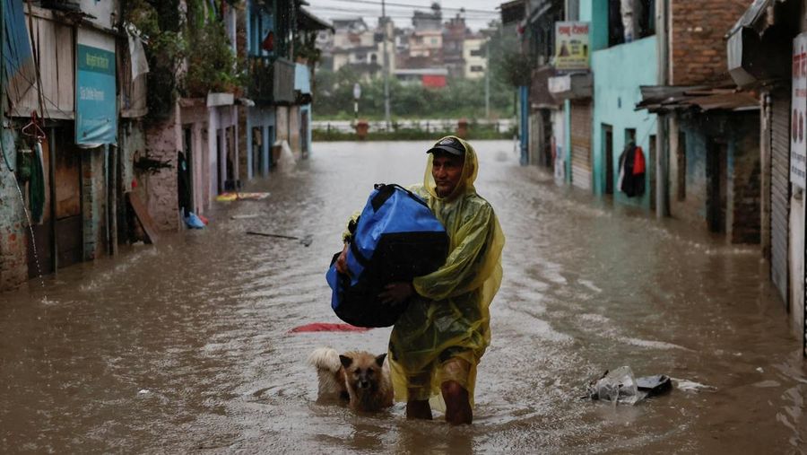 Seorang pria membawa payung berjalan melewati grafiti bertuliskan 'Nepal' di jalan yang banjir di sepanjang tepi Sungai Bagmati yang meluap setelah hujan lebat, di Kathmandu, Nepal, 4 Oktober 2025. (REUTERS/Navesh Chitrakar)