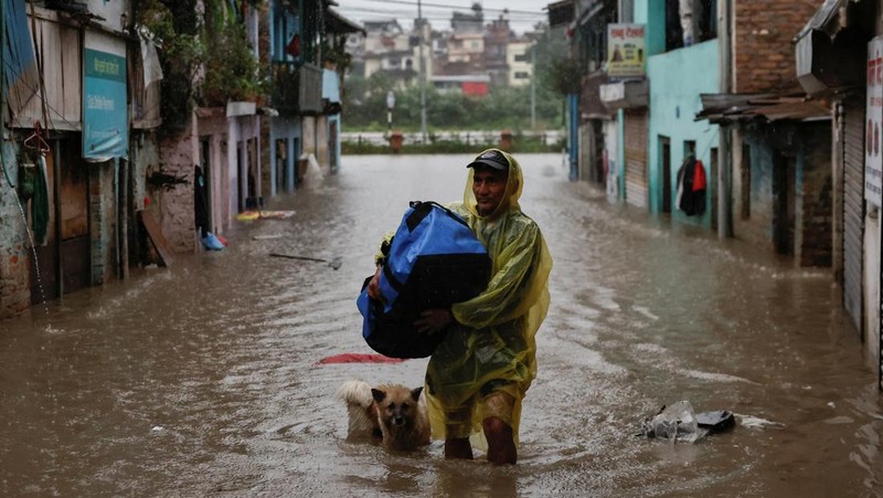 Seorang pria membawa payung berjalan melewati grafiti bertuliskan 'Nepal' di jalan yang banjir di sepanjang tepi Sungai Bagmati yang meluap setelah hujan lebat, di Kathmandu, Nepal, 4 Oktober 2025. (REUTERS/Navesh Chitrakar)