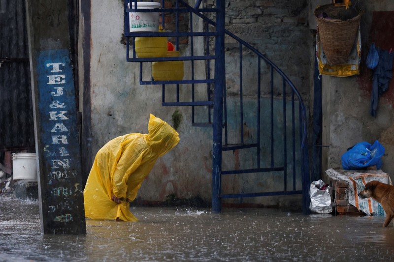 Seorang pria membawa payung berjalan melewati grafiti bertuliskan 'Nepal' di jalan yang banjir di sepanjang tepi Sungai Bagmati yang meluap setelah hujan lebat, di Kathmandu, Nepal, 4 Oktober 2025. (REUTERS/Navesh Chitrakar)
