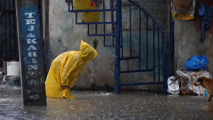 Seorang wanita mengenakan jas hujan berjalan melalui jalan yang banjir di sepanjang tepi Sungai Bagmati yang meluap setelah hujan lebat, di Kathmandu, Nepal, 4 Oktober 2025. (REUTERS/Navesh Chitrakar)