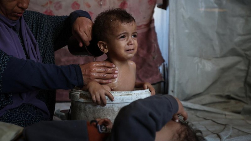 Foto Kombinasi, foto Kiri: Seorang wanita Palestina Iman Abdel Halim Abu Mutlaq menggendong bayi kembarnya yang baru lahir, Uday dan Hamza Abu Odah, di bangsal bersalin di Rumah Sakit Nasser, Khan Younis, Jalur Gaza selatan, 2 November 2023 dua tahun lalu. 
Foto Kanan: Iman Abdel Halim Abu Mutlaq menggendong putra kembarnya Uday dan Hamza Abu Odah di tenda tempat mereka berlindung, di daerah Mawasi, di Khan Younis di Jalur Gaza selatan, 18 September 2025.  (REUTERS/Mohammed Salem-Ramadan Abed)