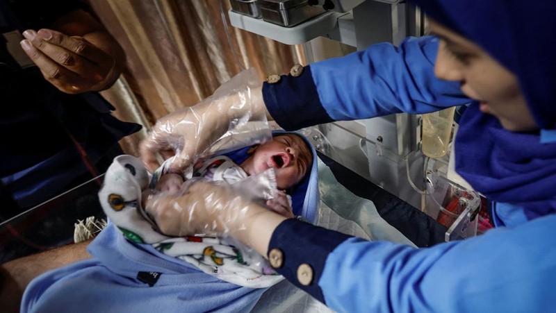Foto Kombinasi, foto Kiri: Seorang wanita Palestina Iman Abdel Halim Abu Mutlaq menggendong bayi kembarnya yang baru lahir, Uday dan Hamza Abu Odah, di bangsal bersalin di Rumah Sakit Nasser, Khan Younis, Jalur Gaza selatan, 2 November 2023 dua tahun lalu. 
Foto Kanan: Iman Abdel Halim Abu Mutlaq menggendong putra kembarnya Uday dan Hamza Abu Odah di tenda tempat mereka berlindung, di daerah Mawasi, di Khan Younis di Jalur Gaza selatan, 18 September 2025.  (REUTERS/Mohammed Salem-Ramadan Abed)