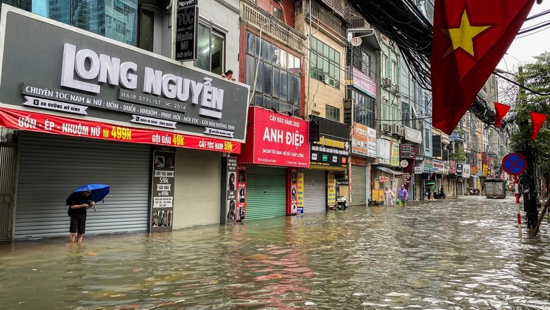 Orang-orang berjalan melalui jalan yang banjir di tengah hujan lebat akibat Topan Matmo, yang menyebabkan kendaraan terlantar, menutup sekolah, memindahkan kelas daring, dan menunda penerbangan ke dan dari Bandara Internasional Noi Bai, di Hanoi, Vietnam, 7 Oktober 2025. (REUTERS/Thinh Tien Nguyen)