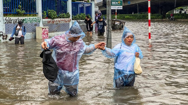 Orang-orang berjalan melalui jalan yang banjir di tengah hujan lebat akibat Topan Matmo, yang menyebabkan kendaraan terlantar, menutup sekolah, memindahkan kelas daring, dan menunda penerbangan ke dan dari Bandara Internasional Noi Bai, di Hanoi, Vietnam, 7 Oktober 2025. (REUTERS/Thinh Tien Nguyen)