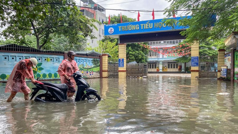 Orang-orang berjalan melalui jalan yang banjir di tengah hujan lebat akibat Topan Matmo, yang menyebabkan kendaraan terlantar, menutup sekolah, memindahkan kelas daring, dan menunda penerbangan ke dan dari Bandara Internasional Noi Bai, di Hanoi, Vietnam, 7 Oktober 2025. (REUTERS/Thinh Tien Nguyen)