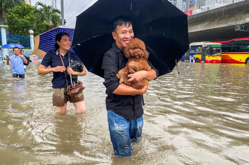 Orang-orang berjalan melalui jalan yang banjir di tengah hujan lebat akibat Topan Matmo, yang menyebabkan kendaraan terlantar, menutup sekolah, memindahkan kelas daring, dan menunda penerbangan ke dan dari Bandara Internasional Noi Bai, di Hanoi, Vietnam, 7 Oktober 2025. (REUTERS/Thinh Tien Nguyen)