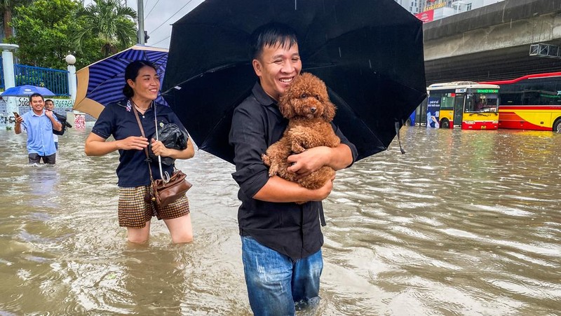 Orang-orang berjalan melalui jalan yang banjir di tengah hujan lebat akibat Topan Matmo, yang menyebabkan kendaraan terlantar, menutup sekolah, memindahkan kelas daring, dan menunda penerbangan ke dan dari Bandara Internasional Noi Bai, di Hanoi, Vietnam, 7 Oktober 2025. (REUTERS/Thinh Tien Nguyen)