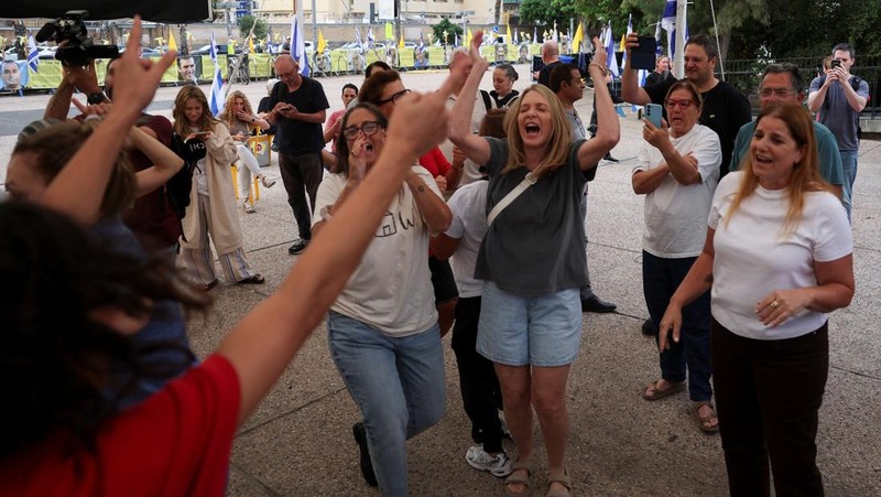 Seorang pria mengenakan topeng bergambar Presiden AS Donald Trump memegang bendera Israel dan balon berbentuk hati, sementara orang-orang merayakan setelah Trump mengumumkan bahwa Israel dan Hamas menyepakati fase pertama gencatan senjata Gaza, di 