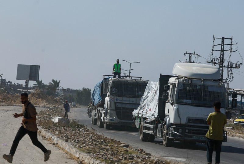 Para relawan Mesir beristirahat dan duduk di samping truk-truk yang membawa bantuan kemanusiaan dari Aliansi Nasional Mesir untuk Pekerjaan Pembangunan Sipil (NACDW) saat mereka menuju perbatasan Rafah untuk memasuki Gaza, setelah gencatan senjata antara Israel dan Hamas di Gaza berlaku, di jalan gurun Kairo-Ismailia, Mesir, 16 Oktober 2025. (REUTERS/Amr Abdallah Dalsh)