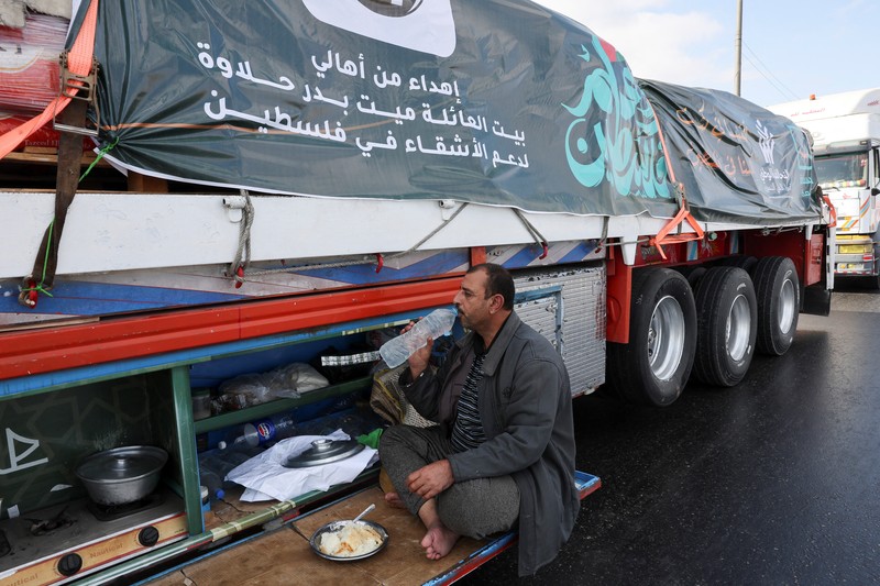 Para relawan Mesir beristirahat dan duduk di samping truk-truk yang membawa bantuan kemanusiaan dari Aliansi Nasional Mesir untuk Pekerjaan Pembangunan Sipil (NACDW) saat mereka menuju perbatasan Rafah untuk memasuki Gaza, setelah gencatan senjata antara Israel dan Hamas di Gaza berlaku, di jalan gurun Kairo-Ismailia, Mesir, 16 Oktober 2025. (REUTERS/Amr Abdallah Dalsh)