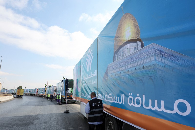 Para relawan Mesir beristirahat dan duduk di samping truk-truk yang membawa bantuan kemanusiaan dari Aliansi Nasional Mesir untuk Pekerjaan Pembangunan Sipil (NACDW) saat mereka menuju perbatasan Rafah untuk memasuki Gaza, setelah gencatan senjata antara Israel dan Hamas di Gaza berlaku, di jalan gurun Kairo-Ismailia, Mesir, 16 Oktober 2025. (REUTERS/Amr Abdallah Dalsh)