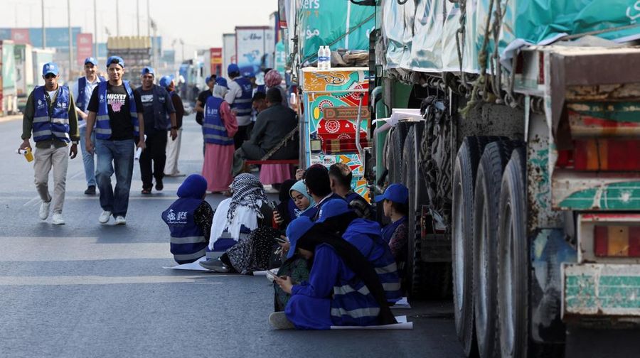 Para relawan Mesir beristirahat dan duduk di samping truk-truk yang membawa bantuan kemanusiaan dari Aliansi Nasional Mesir untuk Pekerjaan Pembangunan Sipil (NACDW) saat mereka menuju perbatasan Rafah untuk memasuki Gaza, setelah gencatan senjata antara Israel dan Hamas di Gaza berlaku, di jalan gurun Kairo-Ismailia, Mesir, 16 Oktober 2025. (REUTERS/Amr Abdallah Dalsh)