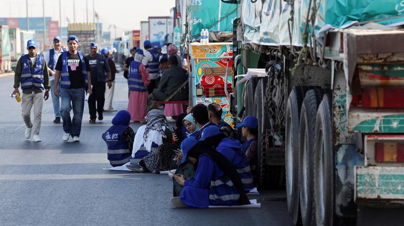 Para relawan Mesir beristirahat dan duduk di samping truk-truk yang membawa bantuan kemanusiaan dari Aliansi Nasional Mesir untuk Pekerjaan Pembangunan Sipil (NACDW) saat mereka menuju perbatasan Rafah untuk memasuki Gaza, setelah gencatan senjata antara Israel dan Hamas di Gaza berlaku, di jalan gurun Kairo-Ismailia, Mesir, 16 Oktober 2025. (REUTERS/Amr Abdallah Dalsh)
