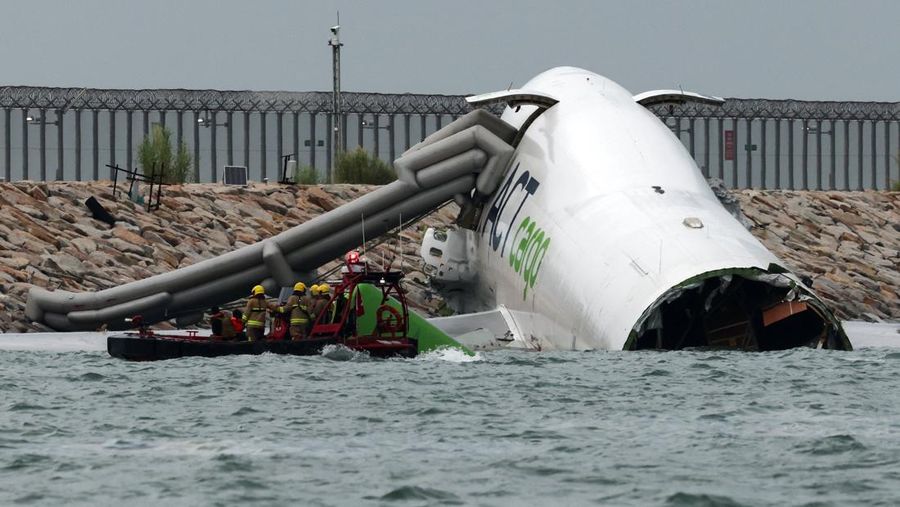 Petugas darurat bekerja di dekat pesawat kargo yang sebagian berada di laut setelah keluar landasan saat mendarat di Bandara Internasional Hong Kong di Hong Kong, Cina, 20 Oktober 2025. (REUTERS/Tyrone Siu)