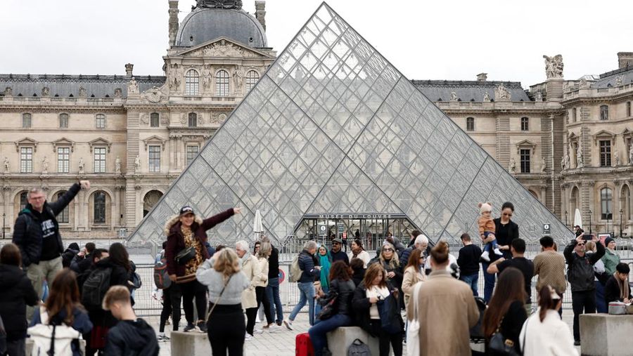 Orang-orang berdiri di dekat Piramida kaca Museum Louvre saat museum tetap tutup sehari setelah perampokan perhiasan spektakuler oleh pencuri yang membobol landmark tersebut dengan menggunakan derek dan memecahkan jendela lantai atas, mencuri perhiasan tak ternilai dari area yang menyimpan permata mahkota Prancis sebelum melarikan diri dengan sepeda motor, di Paris, Prancis, 20 Oktober 2025. (REUTERS/Benoit Tessier)