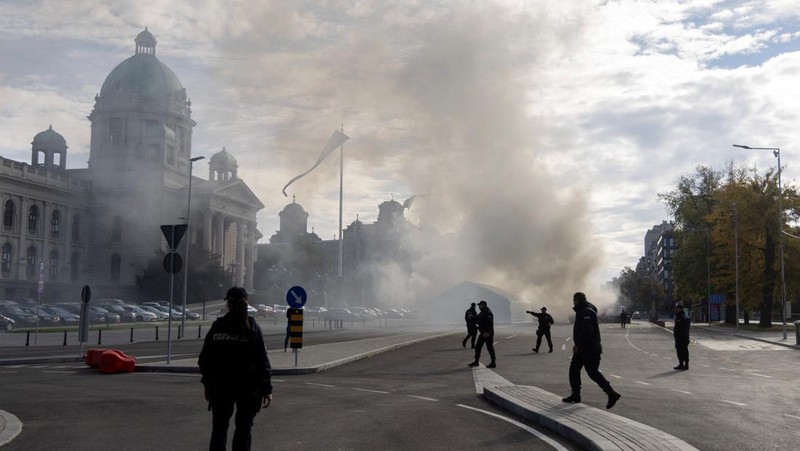 Petugas polisi mengamankan area saat asap mengepul dari tenda yang terbakar menyusul insiden di depan Parlemen di Beograd, Serbia, 22 Oktober 2025. (REUTERS/Djordje Kojadinovic)