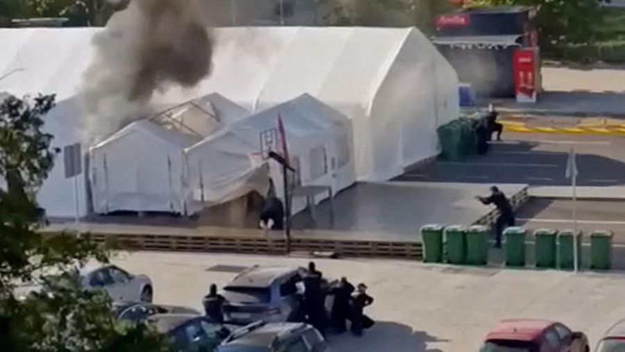 Petugas polisi mengamankan area saat asap mengepul dari tenda yang terbakar menyusul insiden di depan Parlemen di Beograd, Serbia, 22 Oktober 2025. (REUTERS/Djordje Kojadinovic)