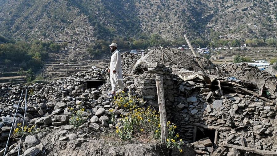 Seorang pria Afghanistan berdiri di atas sisa-sisa rumah yang rusak akibat gempa bumi bulan September di desa Mazar Dara di distrik Nurgal, provinsi Kunar pada tanggal 29 Oktober 2025. (Photo by Wakil KOHSAR / AFP)