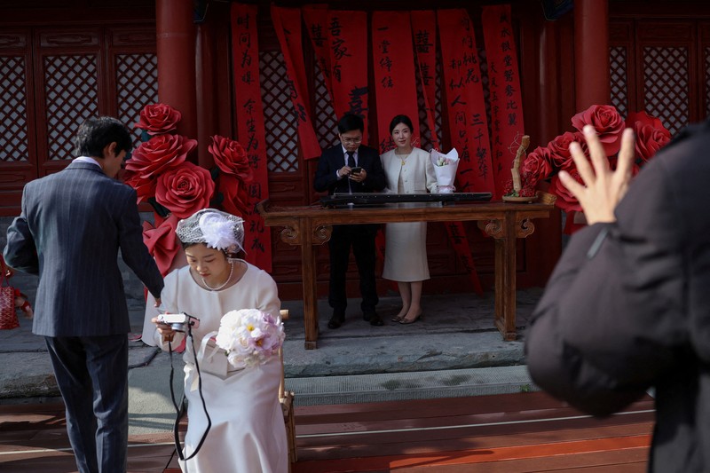 Wang Jieyu, 31, dan Zhan Yongqiang, 33, berpose untuk seorang fotografer dengan surat nikah mereka setelah mereka mendaftar di Kuil Huguo Guanyin, di Beijing, Tiongkok, 28 Oktober 2025. (REUTERS/Tingshu Wang)