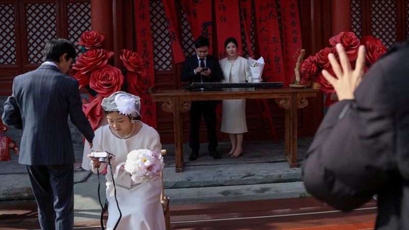 Wang Jieyu, 31, dan Zhan Yongqiang, 33, berpose untuk seorang fotografer dengan surat nikah mereka setelah mereka mendaftar di Kuil Huguo Guanyin, di Beijing, Tiongkok, 28 Oktober 2025. (REUTERS/Tingshu Wang)