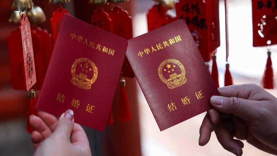Wang Jieyu, 31, dan Zhan Yongqiang, 33, berpose untuk seorang fotografer dengan surat nikah mereka setelah mereka mendaftar di Kuil Huguo Guanyin, di Beijing, Tiongkok, 28 Oktober 2025. (REUTERS/Tingshu Wang)