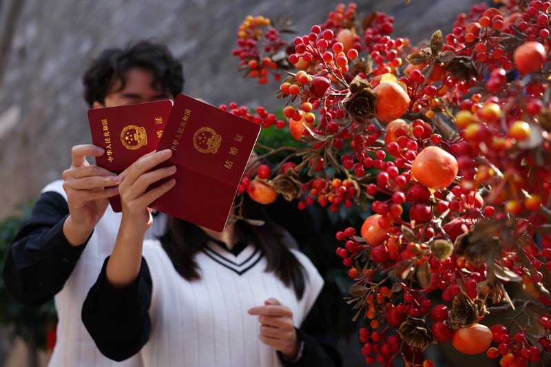 Wang Jieyu, 31, dan Zhan Yongqiang, 33, berpose untuk seorang fotografer dengan surat nikah mereka setelah mereka mendaftar di Kuil Huguo Guanyin, di Beijing, Tiongkok, 28 Oktober 2025. (REUTERS/Tingshu Wang)
