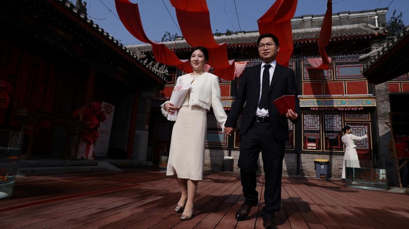 Wang Jieyu, 31, dan Zhan Yongqiang, 33, berpose untuk seorang fotografer dengan surat nikah mereka setelah mereka mendaftar di Kuil Huguo Guanyin, di Beijing, Tiongkok, 28 Oktober 2025. (REUTERS/Tingshu Wang)