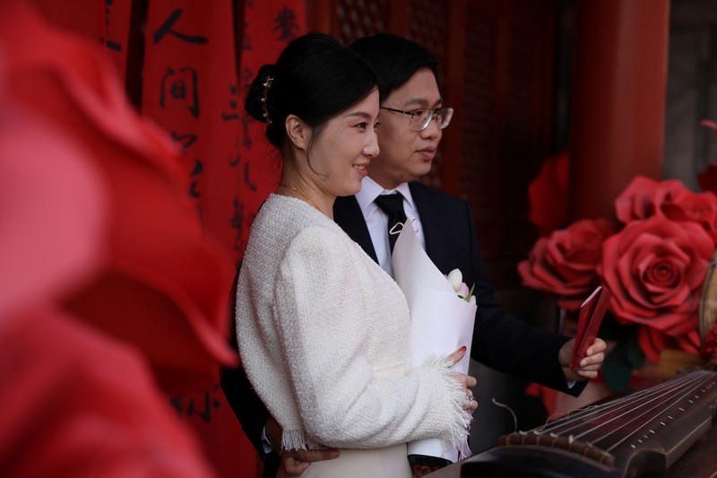 Wang Jieyu, 31, dan Zhan Yongqiang, 33, berpose untuk seorang fotografer dengan surat nikah mereka setelah mereka mendaftar di Kuil Huguo Guanyin, di Beijing, Tiongkok, 28 Oktober 2025. (REUTERS/Tingshu Wang)