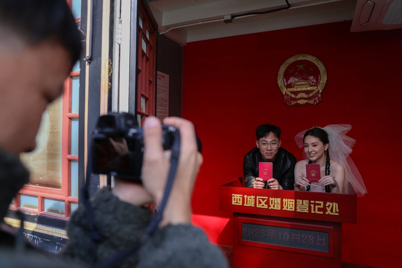 Wang Jieyu, 31, dan Zhan Yongqiang, 33, berpose untuk seorang fotografer dengan surat nikah mereka setelah mereka mendaftar di Kuil Huguo Guanyin, di Beijing, Tiongkok, 28 Oktober 2025. (REUTERS/Tingshu Wang)