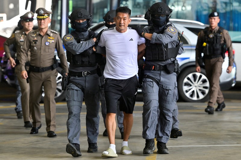 Raja judi asal China, She Zhijiang dikawal oleh Kepolisian Kerajaan Thailand keluar dari Kantor Polisi Bandara Suvarnabhumi di Bangkok, Thailand, Rabu (12/11/2025). (REUTERS/Thanaphon Wuttison)