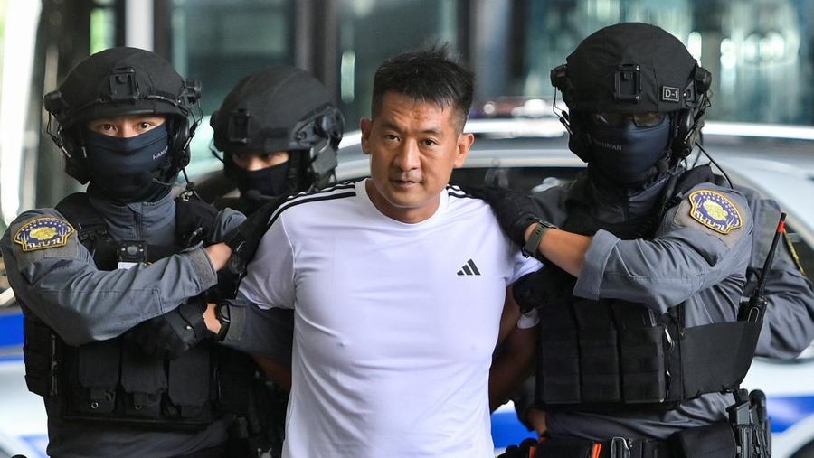 Raja judi asal China, She Zhijiang dikawal oleh Kepolisian Kerajaan Thailand keluar dari Kantor Polisi Bandara Suvarnabhumi di Bangkok, Thailand, Rabu (12/11/2025). (REUTERS/Thanaphon Wuttison)