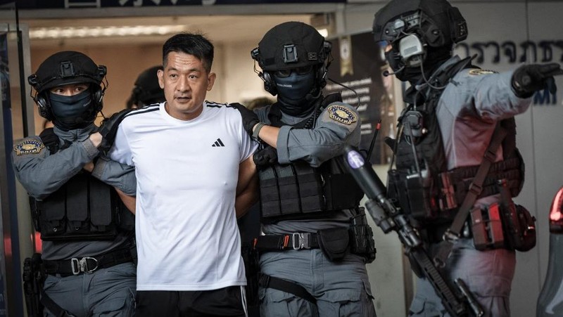 Raja judi asal China, She Zhijiang dikawal oleh Kepolisian Kerajaan Thailand keluar dari Kantor Polisi Bandara Suvarnabhumi di Bangkok, Thailand, Rabu (12/11/2025). (REUTERS/Thanaphon Wuttison)