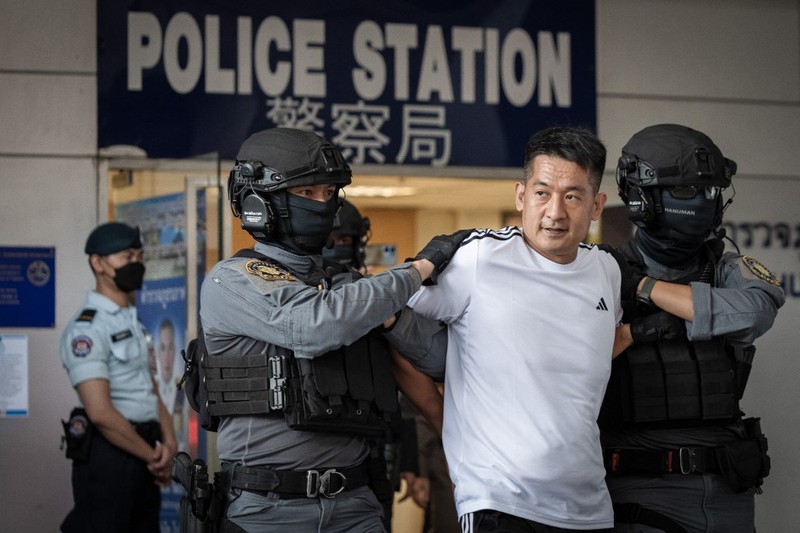 Raja judi asal China, She Zhijiang dikawal oleh Kepolisian Kerajaan Thailand keluar dari Kantor Polisi Bandara Suvarnabhumi di Bangkok, Thailand, Rabu (12/11/2025). (REUTERS/Thanaphon Wuttison)