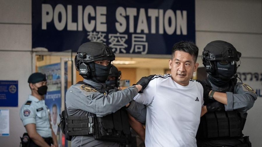 Raja judi asal China, She Zhijiang dikawal oleh Kepolisian Kerajaan Thailand keluar dari Kantor Polisi Bandara Suvarnabhumi di Bangkok, Thailand, Rabu (12/11/2025). (REUTERS/Thanaphon Wuttison)