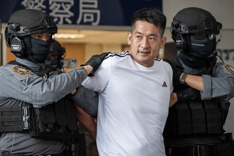 Raja judi asal China, She Zhijiang dikawal oleh Kepolisian Kerajaan Thailand keluar dari Kantor Polisi Bandara Suvarnabhumi di Bangkok, Thailand, Rabu (12/11/2025). (REUTERS/Thanaphon Wuttison)