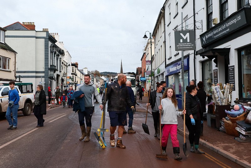Orang-orang membawa sapu dan sekop berjalan di jalan, setelah banjir parah yang disebabkan oleh Badai Claudia, di Monmouth, Wales, Inggris, 16 November 2025. (REUTERS/Isabel Infantes)