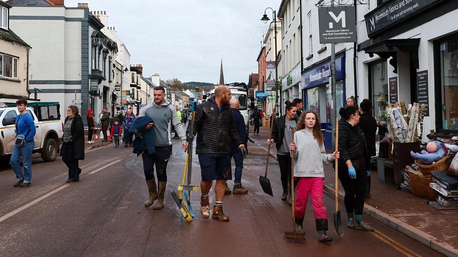 Orang-orang membawa sapu dan sekop berjalan di jalan, setelah banjir parah yang disebabkan oleh Badai Claudia, di Monmouth, Wales, Inggris, 16 November 2025. (REUTERS/Isabel Infantes)
