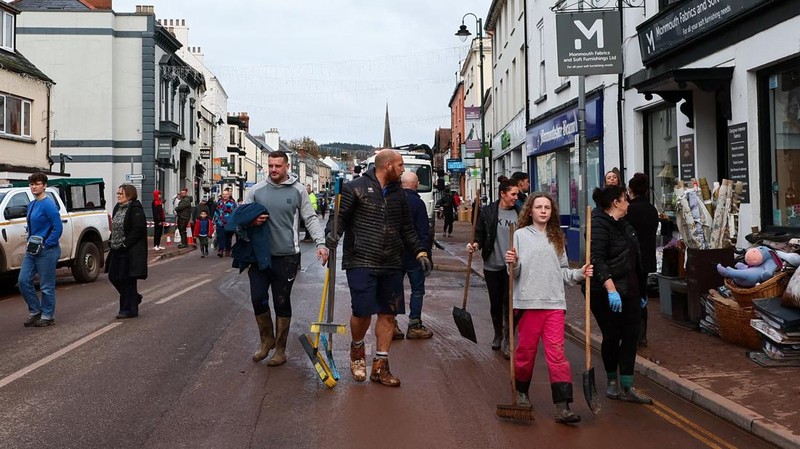 Orang-orang membawa sapu dan sekop berjalan di jalan, setelah banjir parah yang disebabkan oleh Badai Claudia, di Monmouth, Wales, Inggris, 16 November 2025. (REUTERS/Isabel Infantes)