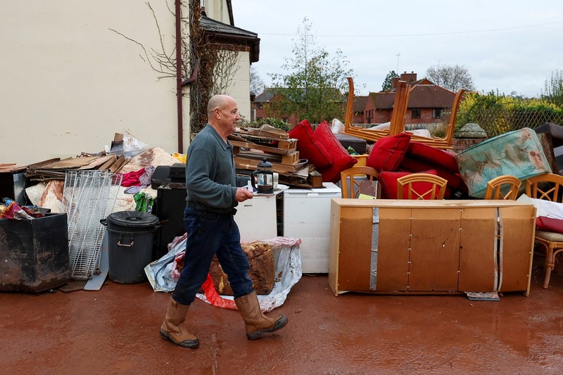 Orang-orang membawa sapu dan sekop berjalan di jalan, setelah banjir parah yang disebabkan oleh Badai Claudia, di Monmouth, Wales, Inggris, 16 November 2025. (REUTERS/Isabel Infantes)
