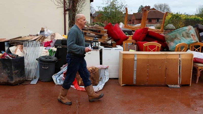 Orang-orang membawa sapu dan sekop berjalan di jalan, setelah banjir parah yang disebabkan oleh Badai Claudia, di Monmouth, Wales, Inggris, 16 November 2025. (REUTERS/Isabel Infantes)