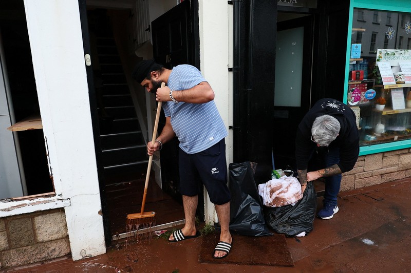 Orang-orang membawa sapu dan sekop berjalan di jalan, setelah banjir parah yang disebabkan oleh Badai Claudia, di Monmouth, Wales, Inggris, 16 November 2025. (REUTERS/Isabel Infantes)