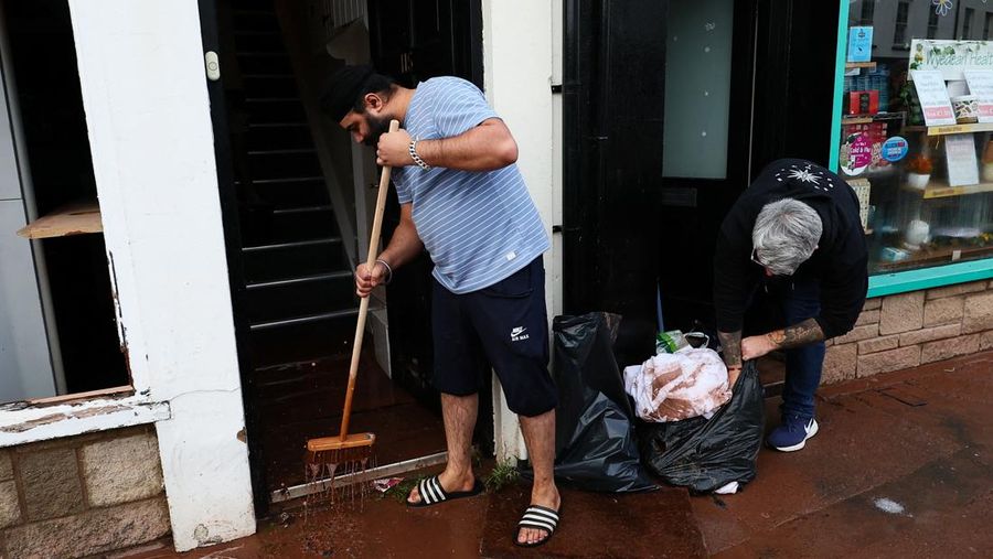 Orang-orang membawa sapu dan sekop berjalan di jalan, setelah banjir parah yang disebabkan oleh Badai Claudia, di Monmouth, Wales, Inggris, 16 November 2025. (REUTERS/Isabel Infantes)