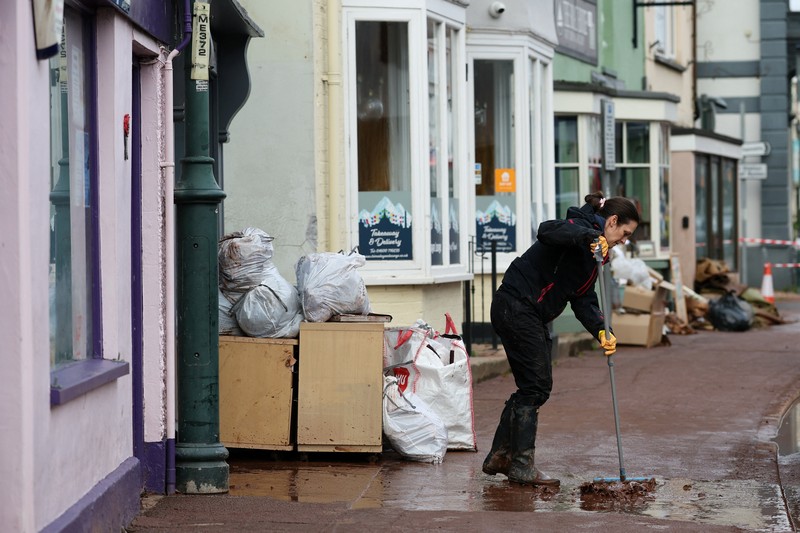 Orang-orang membawa sapu dan sekop berjalan di jalan, setelah banjir parah yang disebabkan oleh Badai Claudia, di Monmouth, Wales, Inggris, 16 November 2025. (REUTERS/Isabel Infantes)