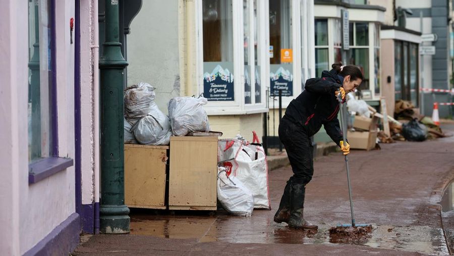 Orang-orang membawa sapu dan sekop berjalan di jalan, setelah banjir parah yang disebabkan oleh Badai Claudia, di Monmouth, Wales, Inggris, 16 November 2025. (REUTERS/Isabel Infantes)