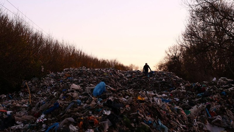 Seorang pria berjalan melewati tumpukan sampah yang dibuang secara ilegal di dataran banjir di sebelah jalan A34, yang memicu penyelidikan Badan Lingkungan Hidup terhadap dugaan kejahatan terorganisir, dekat Kidlington, Oxfordshire, Inggris, 17 November 2025. (REUTERS/Isabel Infantes)
