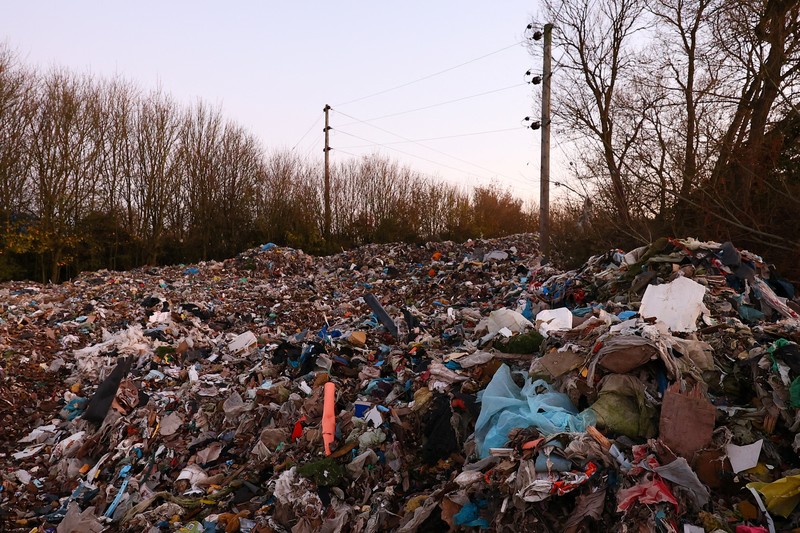 Seorang pria berjalan melewati tumpukan sampah yang dibuang secara ilegal di dataran banjir di sebelah jalan A34, yang memicu penyelidikan Badan Lingkungan Hidup terhadap dugaan kejahatan terorganisir, dekat Kidlington, Oxfordshire, Inggris, 17 November 2025. (REUTERS/Isabel Infantes)