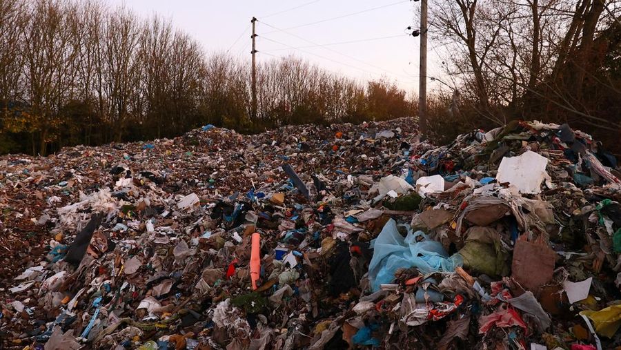 Seorang pria berjalan melewati tumpukan sampah yang dibuang secara ilegal di dataran banjir di sebelah jalan A34, yang memicu penyelidikan Badan Lingkungan Hidup terhadap dugaan kejahatan terorganisir, dekat Kidlington, Oxfordshire, Inggris, 17 November 2025. (REUTERS/Isabel Infantes)